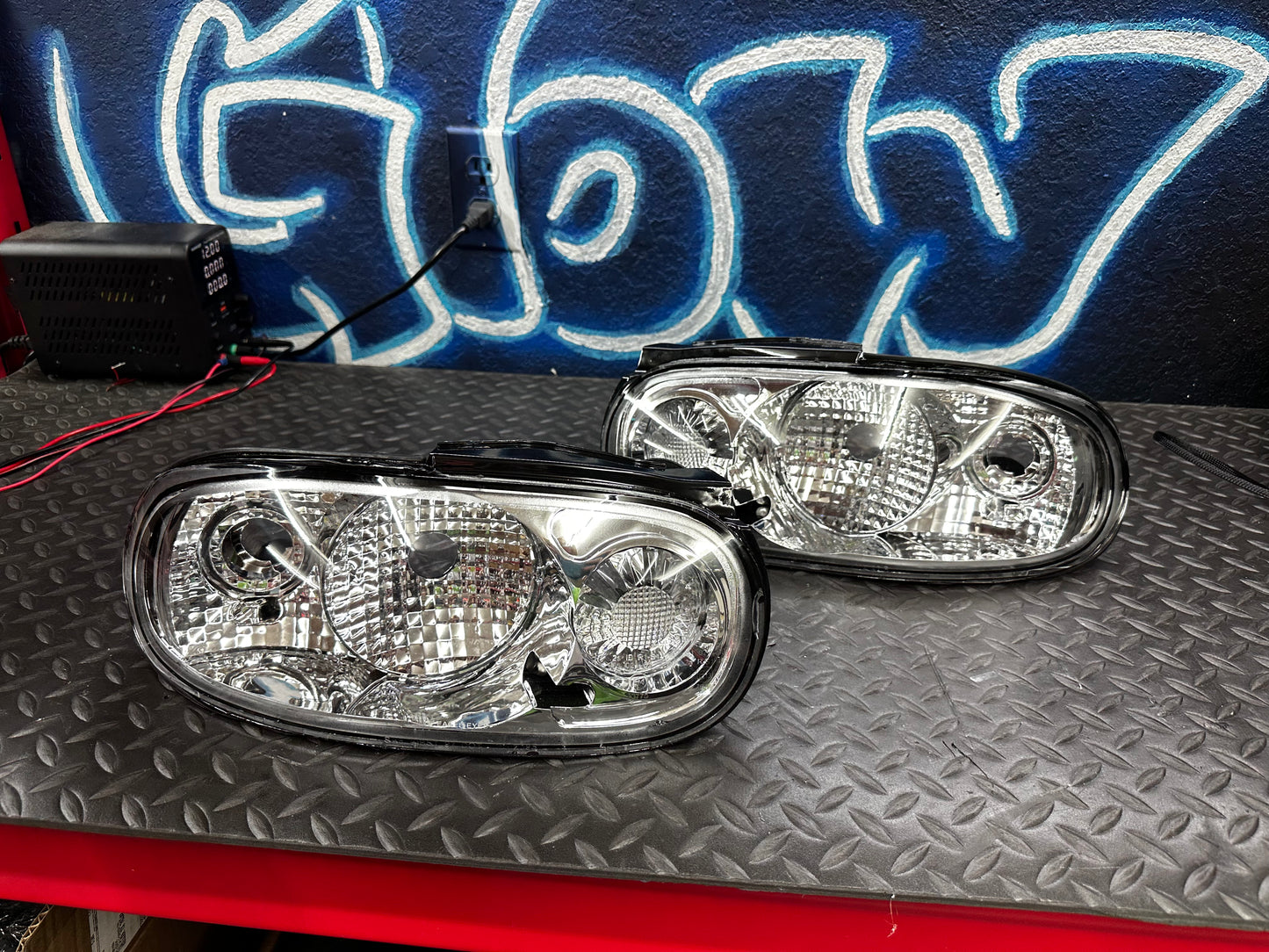Pair of clear tail lights for 1990-1997 NA Mazda Miata on a workbench, sold as-is with disclosed driver-side lens damage
