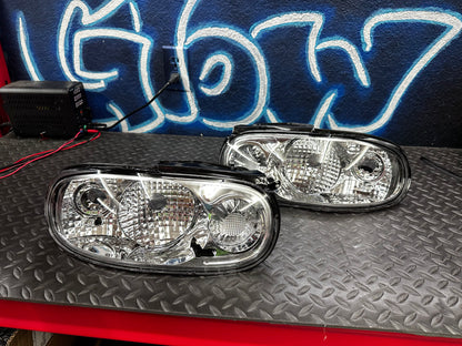 Pair of clear tail lights for 1990-1997 NA Mazda Miata on a workbench, sold as-is with disclosed driver-side lens damage